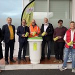 Weiterer Tauschpunkt für Altspeisefett Sieben Männer präsentieren grüne Sammelbehälter vor einer Recyclingtonne.