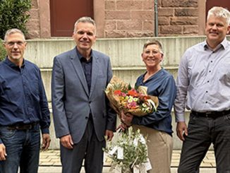 Vier Personen bei einer Blumenübergabe im Freien.