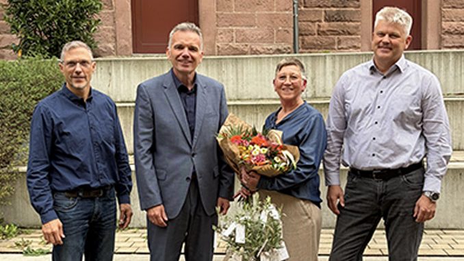 Vier Personen bei einer Blumenübergabe im Freien.