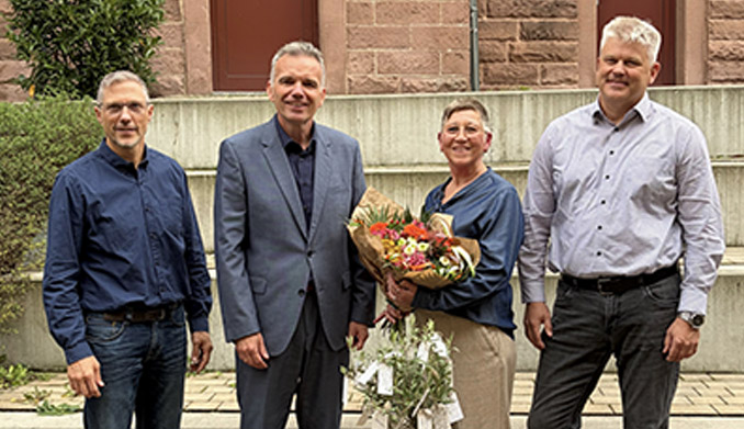 Vier Personen bei einer Blumenübergabe im Freien.