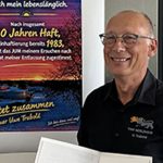 Mann lächelt neben einem Poster zu seiner Haftentlassung.