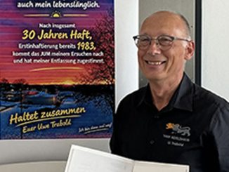 Mann lächelt neben einem Poster zu seiner Haftentlassung.
