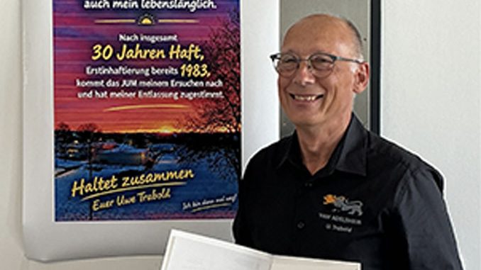 Mann lächelt neben einem Poster zu seiner Haftentlassung.