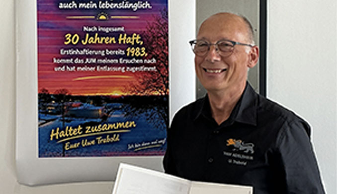 Mann lächelt neben einem Poster zu seiner Haftentlassung.