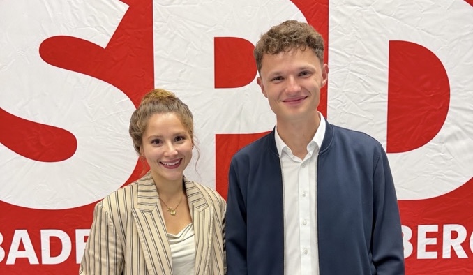 Zwei junge Personen lächelnd vor einem SPD-Hintergrund.